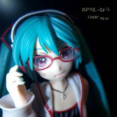 Headshot of a Hatsune Miku doll with headphones and red glasses, she is looking into the camera.
