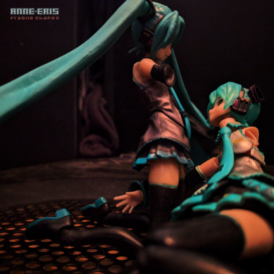 Two identical Hatsune Miku dolls looking into each other's eyes, thee are both missing one arm.